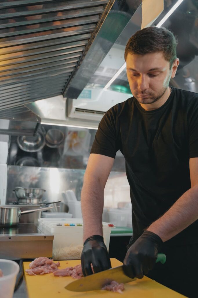 Chef slicing meat on a cutting board in a busy commercial kitchen, showcasing culinary skills.