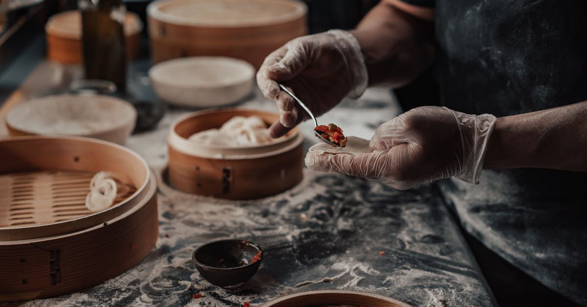 Chef uses gloves to fill dumplings in a kitchen with bamboo steamers and flour dust.